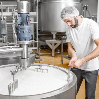 Man mixing milk in the stainless tank during the fermentation process at the cheese manufacturing.jpeg